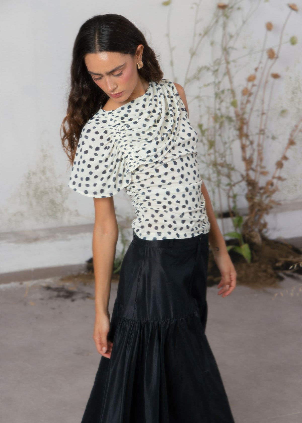 White polka dot ruffle cold-shoulder top with asymmetric drape detail, paired with black satin maxi skirt