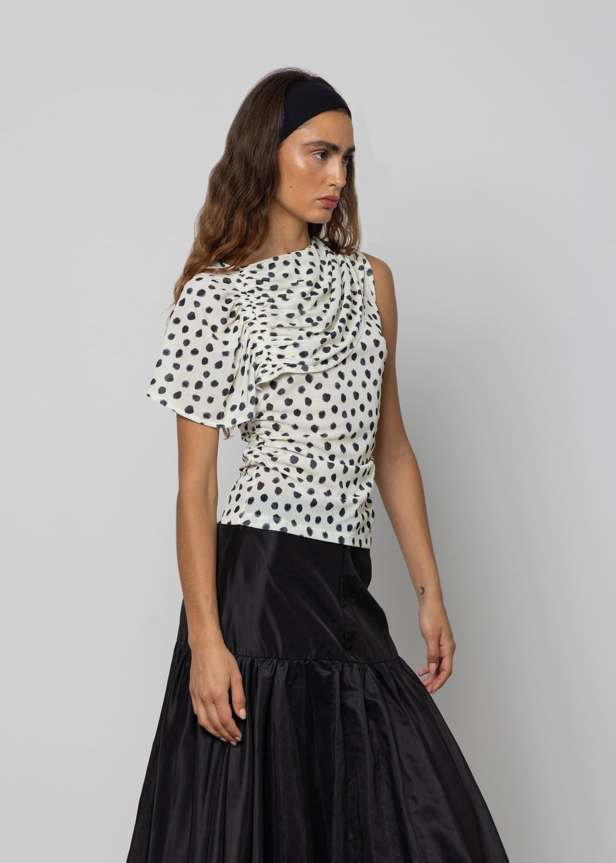 White polka dot ruched one-shoulder top with ruffled detail, paired with a black satin maxi skirt.