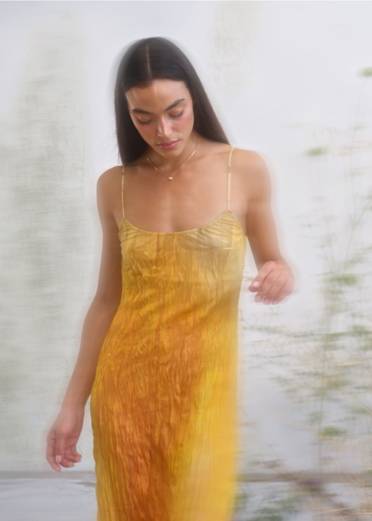 Yellow-orange ombre crinkle slip dress with spaghetti straps, shown in motion on a dark-haired model.