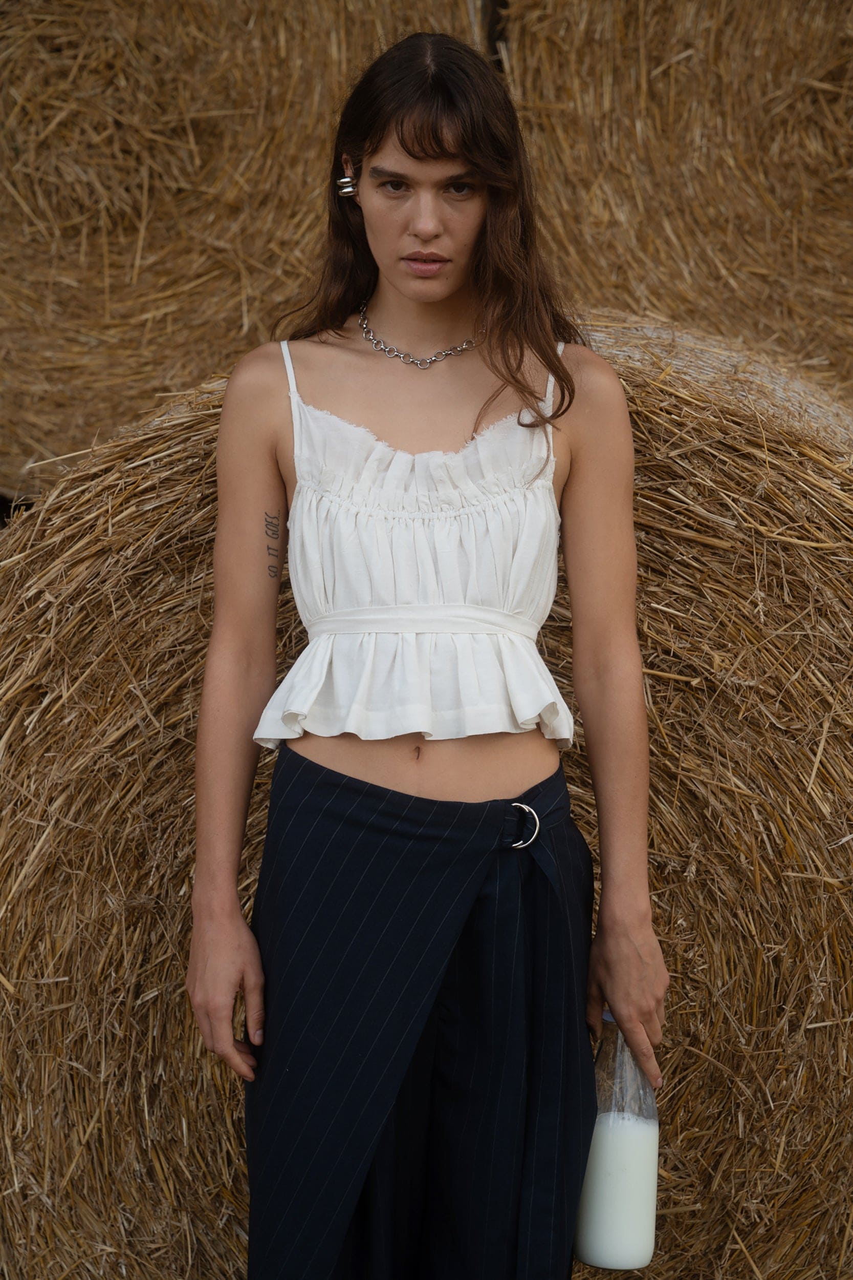 White ruched cotton crop top with thin straps and peplum hem, paired with navy wrap skirt against hay bale backdrop