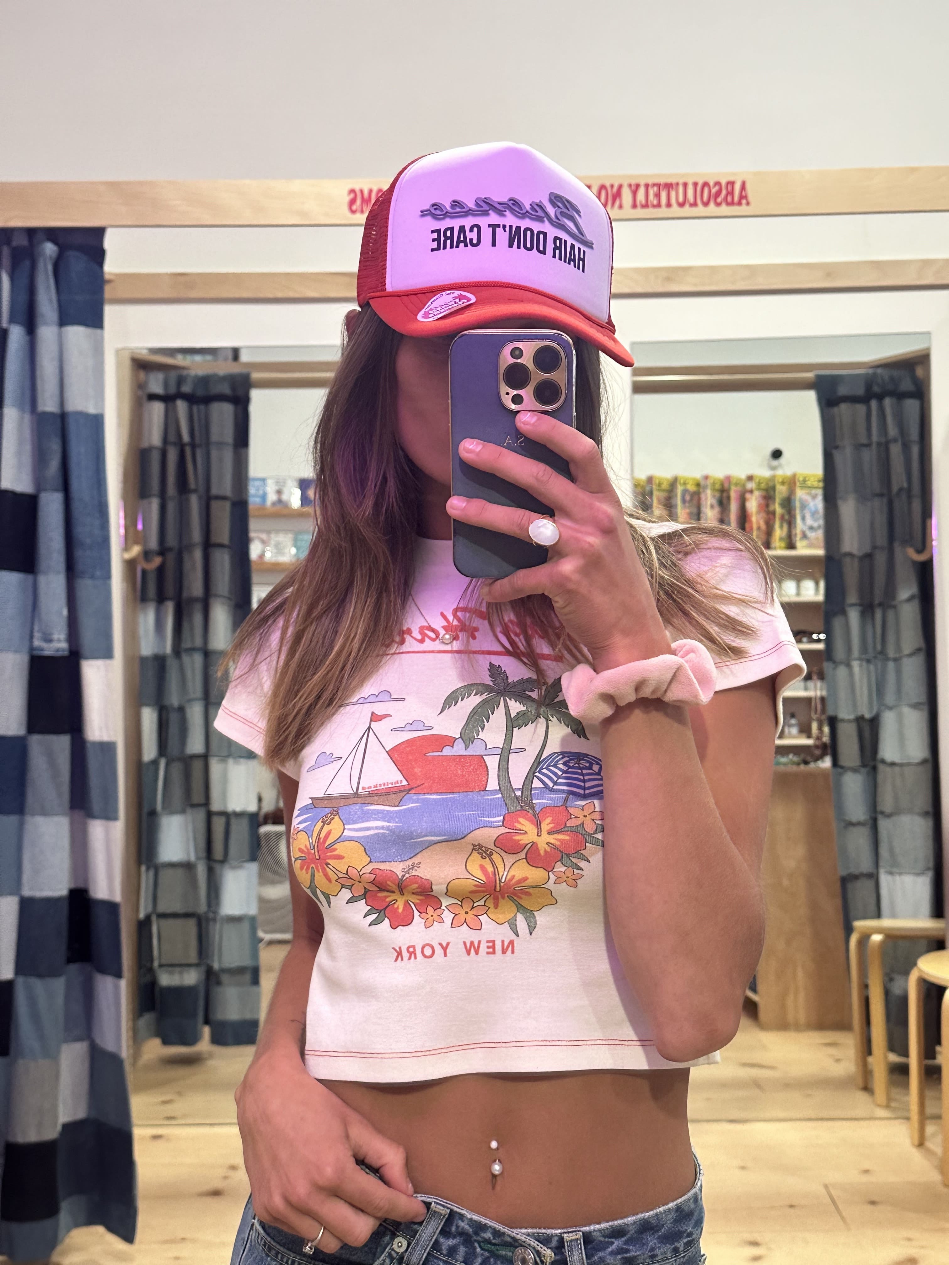 Person holding a phone with a colorful case, wearing a pink cap and floral-patterned shirt.