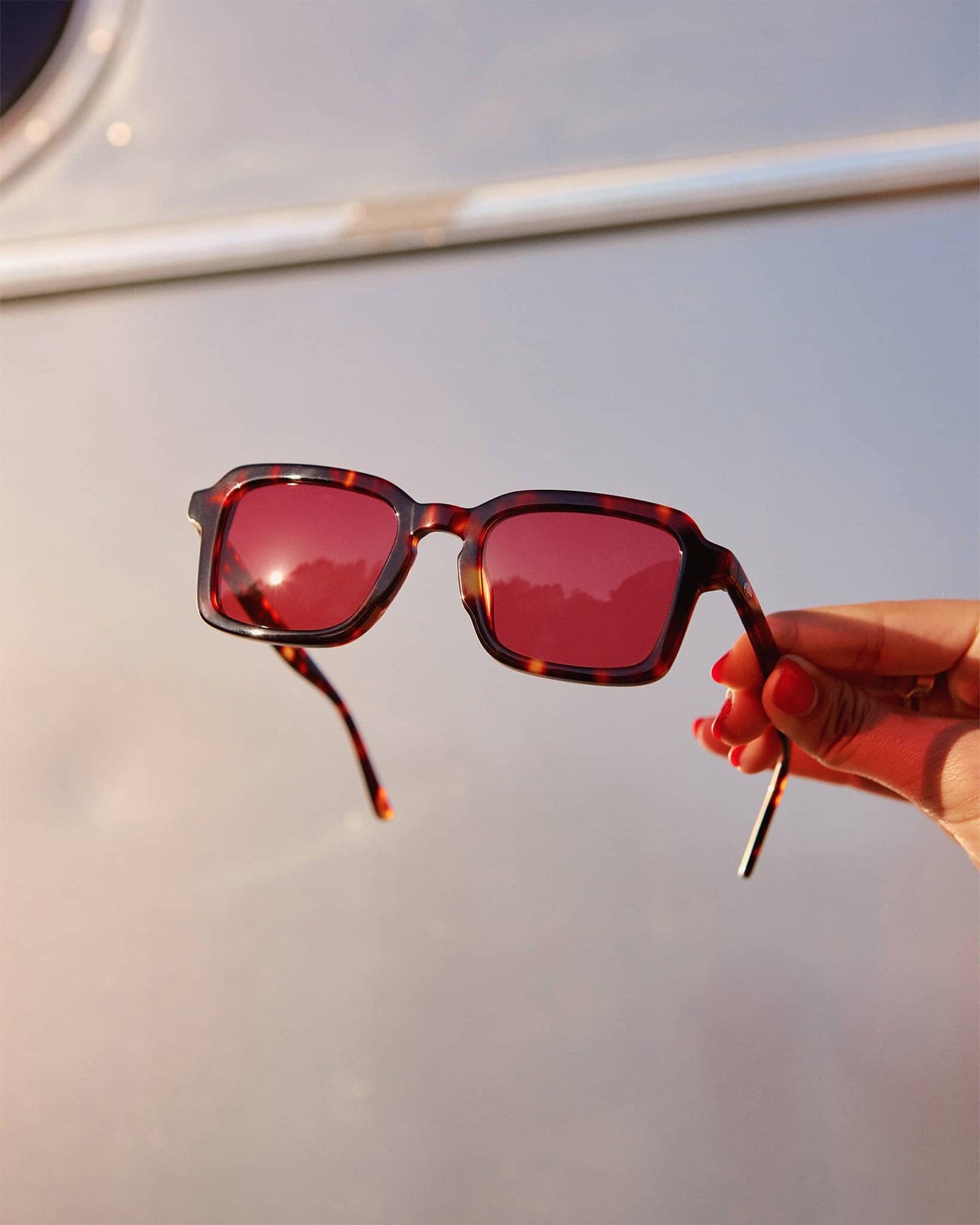 Sunglasses with red lenses held by a hand against a blurred background