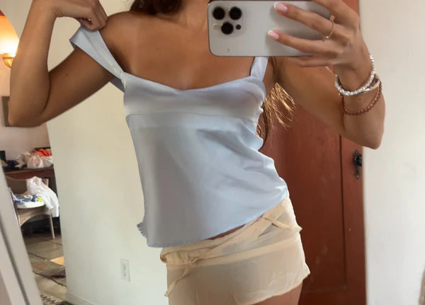 Person taking a mirror selfie wearing a light blue top and beige shorts.