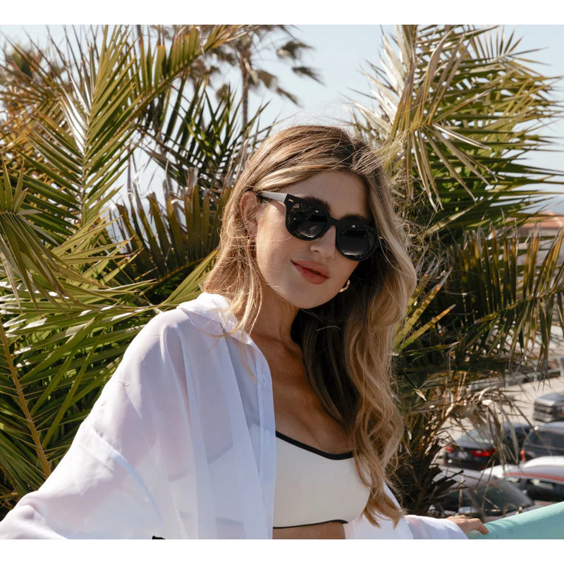 Woman wearing sunglasses and a white outfit with palm trees in the background
