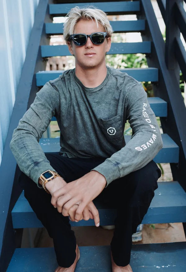 Person wearing sunglasses and a gray long-sleeve shirt with text, sitting on blue steps.