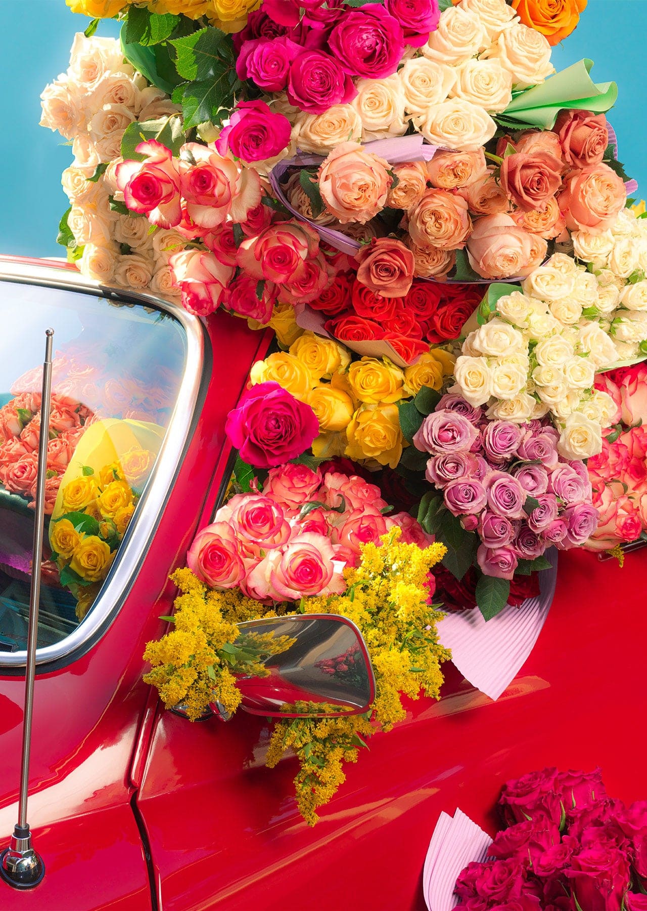 Vibrant bouquets of colorful roses in pink, yellow, peach, white, and red displayed on and around a classic red vintage car