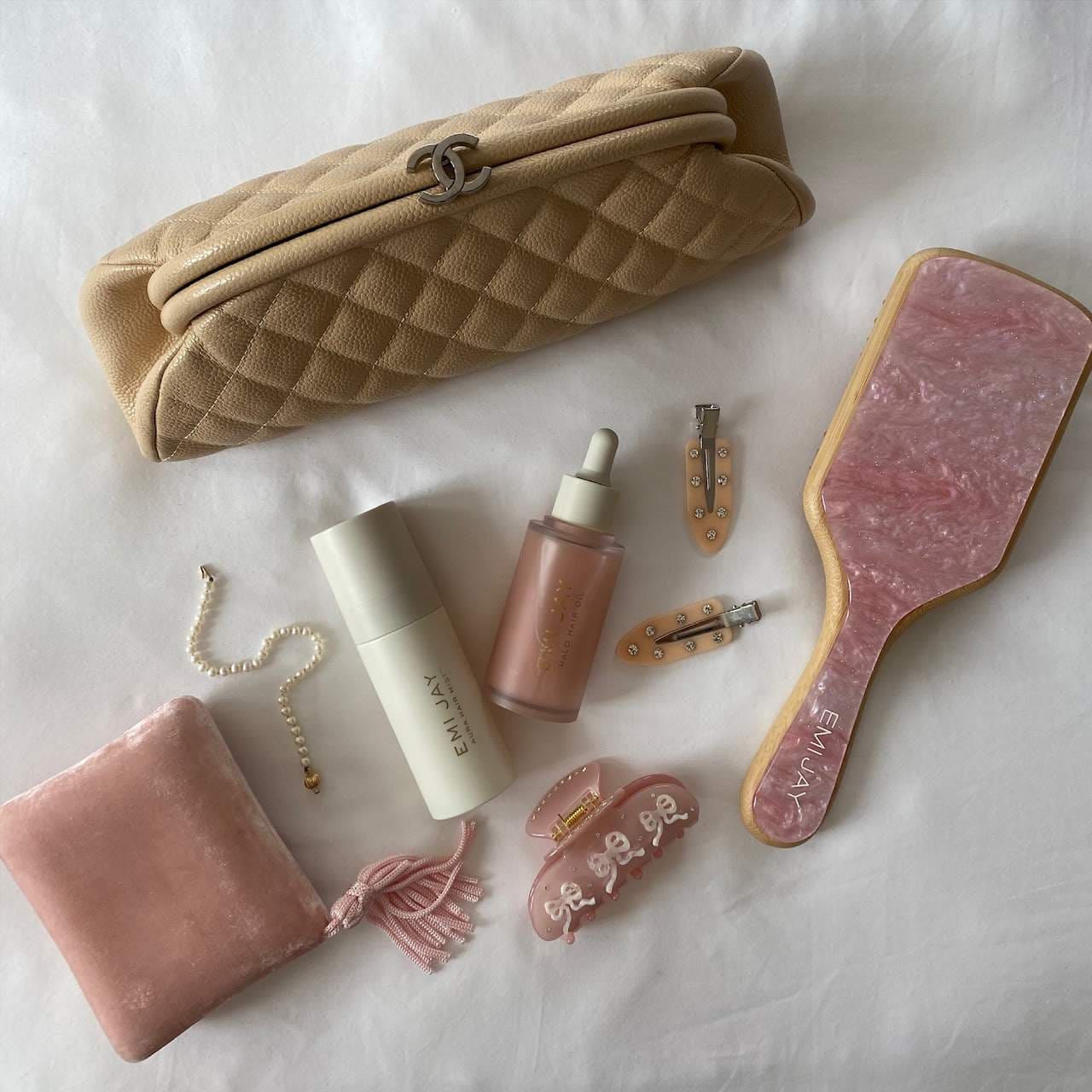 Beige quilted makeup bag with beauty tools including pink gua sha, hair clips, serum bottles, pearl necklace and velvet pouch