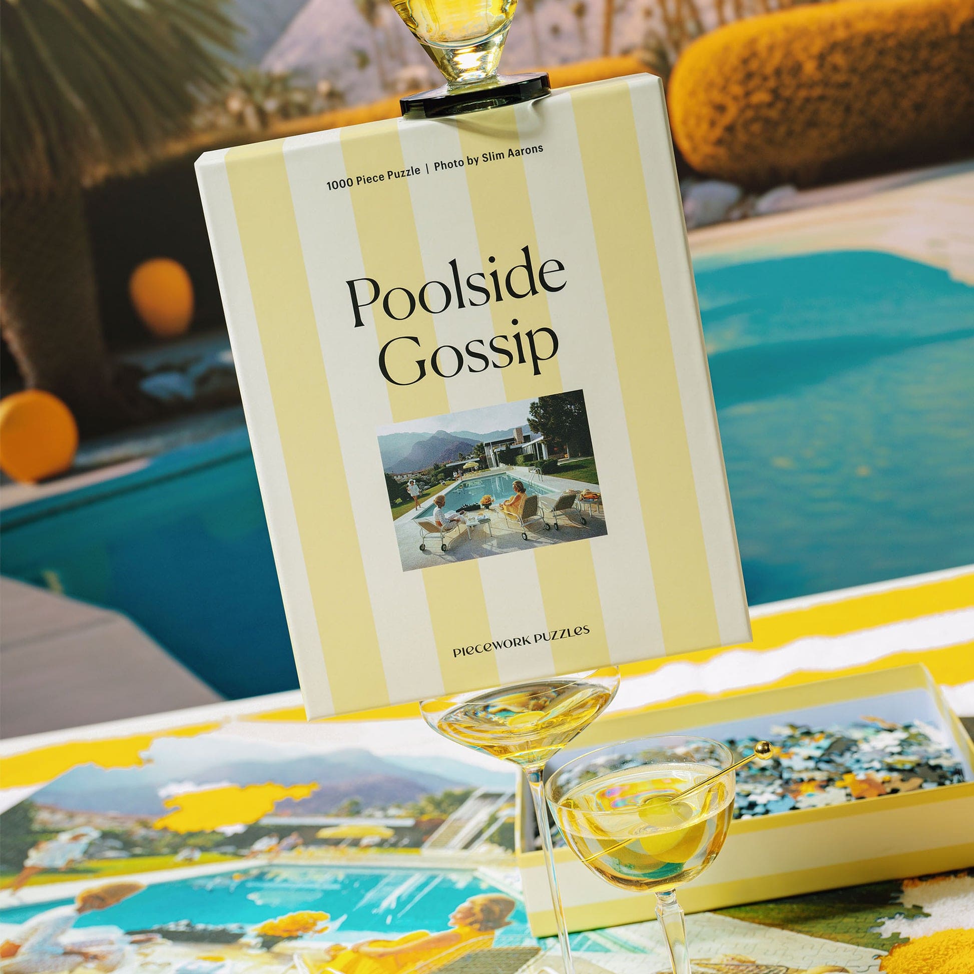 1000-piece jigsaw puzzle box titled "Poolside Gossip" with yellow and white striped design, featuring a mid-century pool scene photo