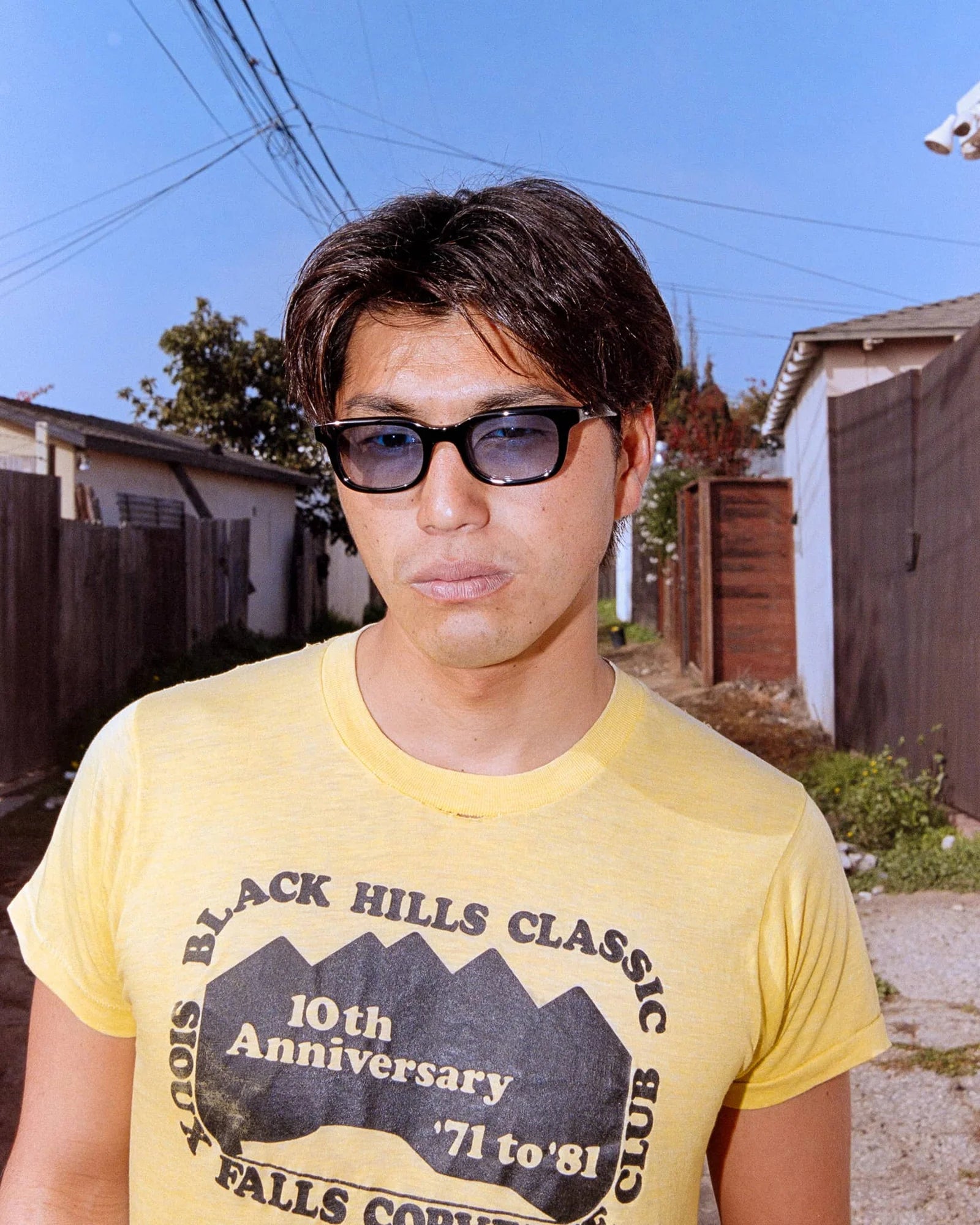 Person wearing sunglasses and a yellow t-shirt with text in an outdoor setting