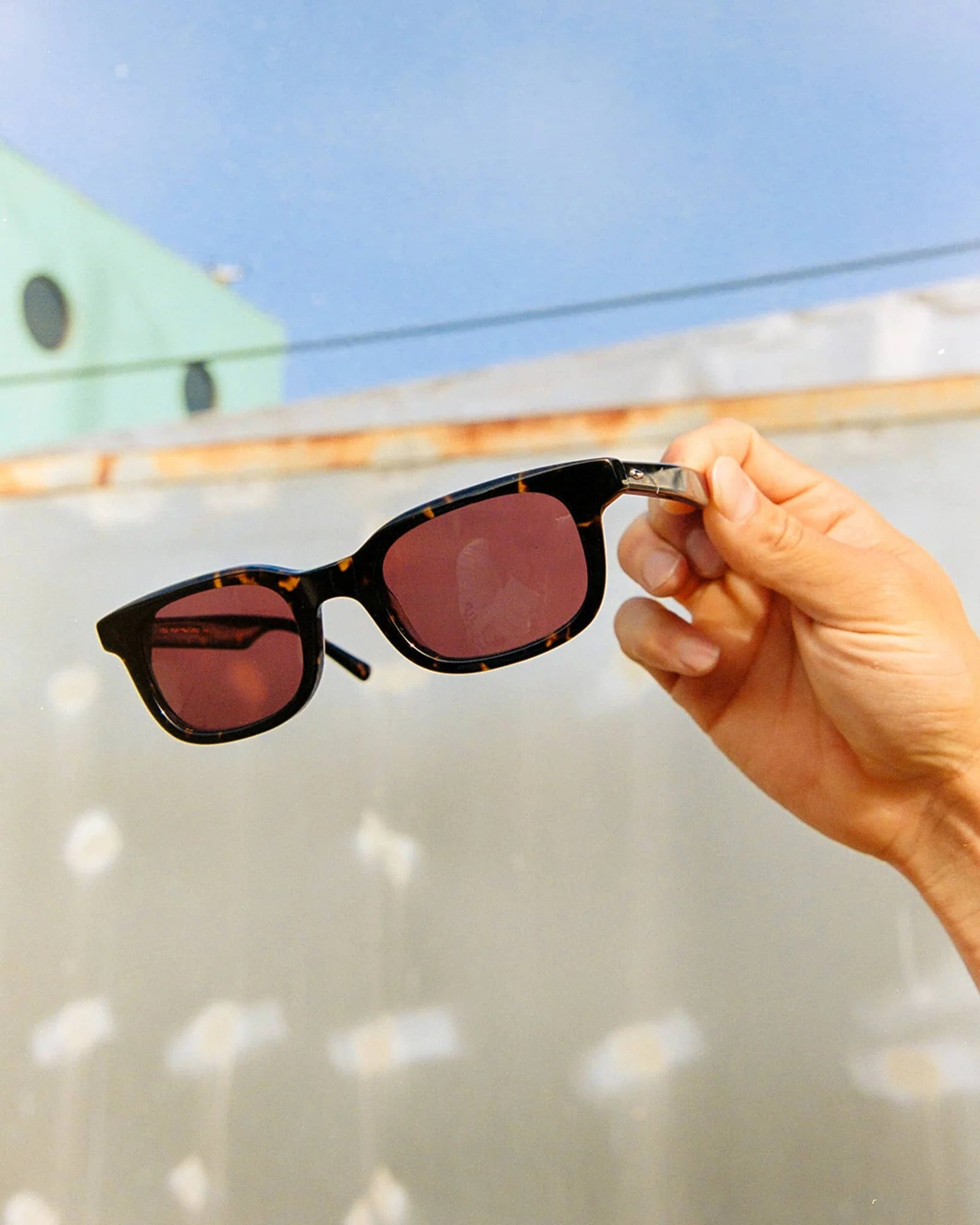 Sunglasses with red lenses held by a hand against a blurred outdoor background