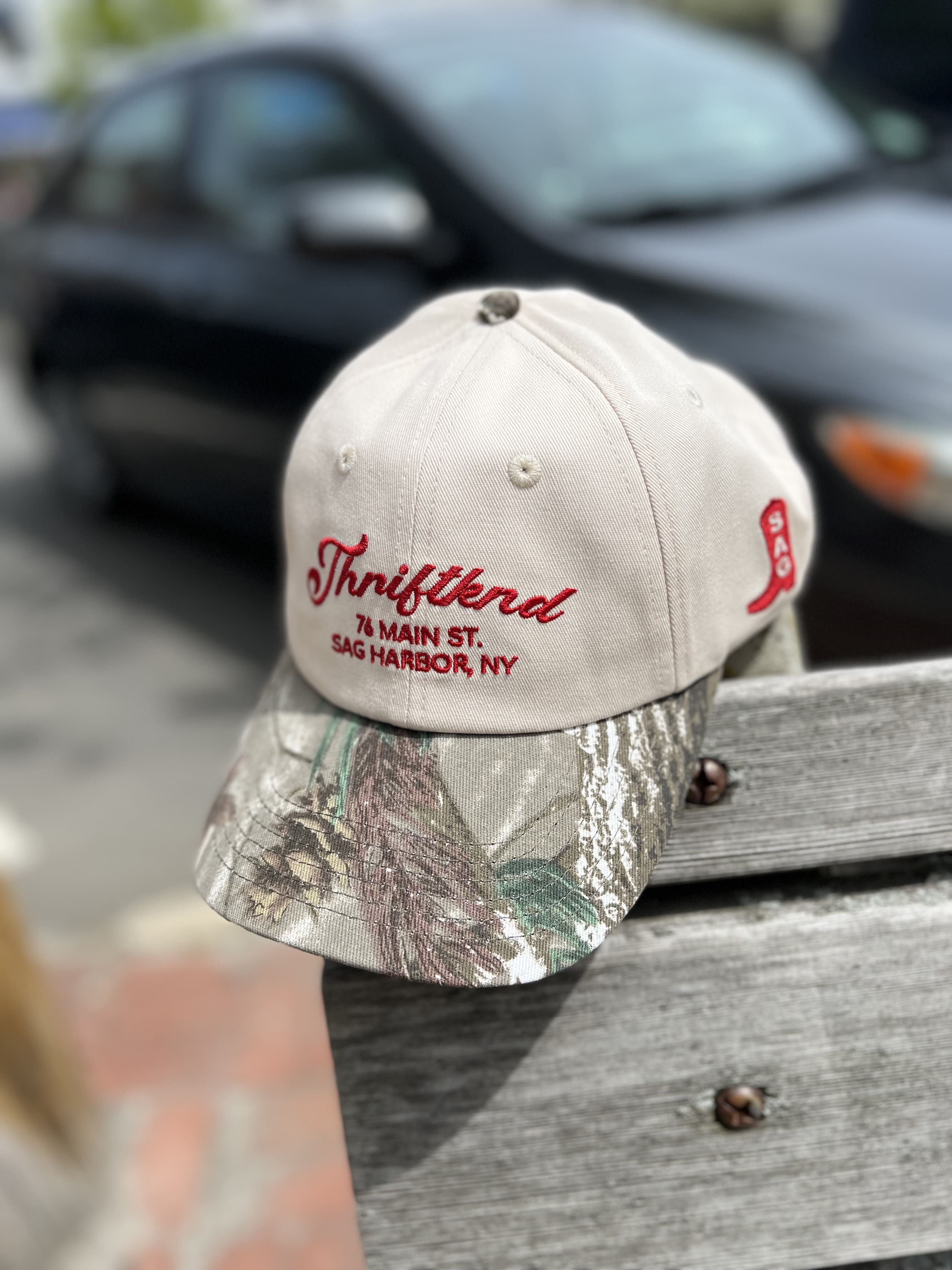 Beige baseball cap with camouflage brim featuring red embroidered text "Thriffland 76 Main St Sag Harbor, NY"