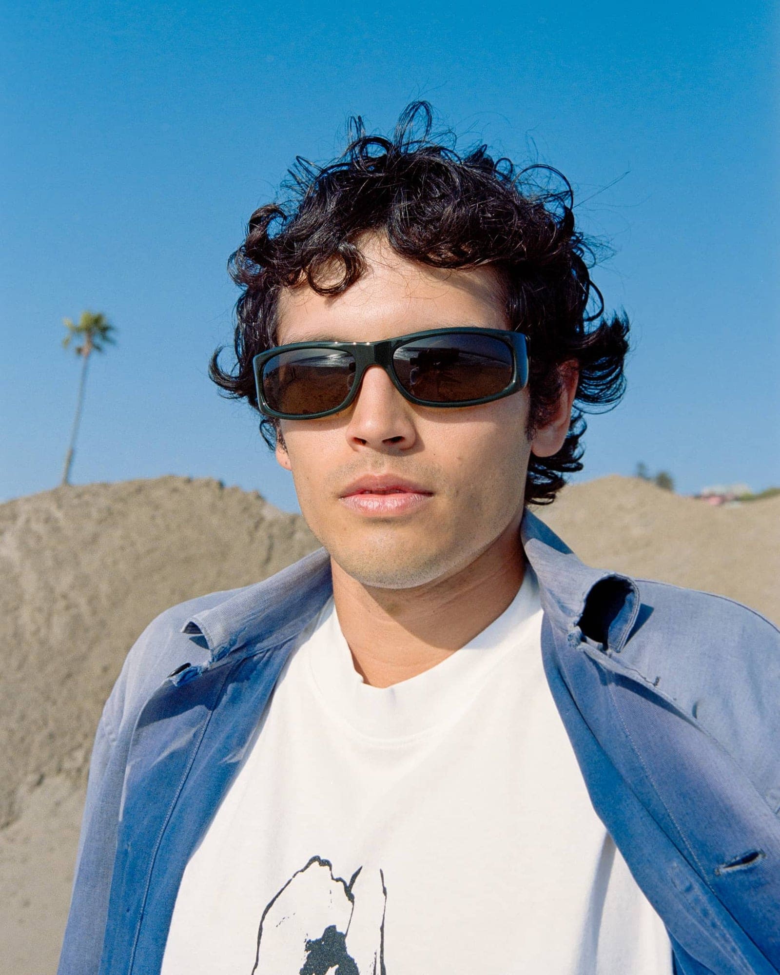 Man wearing sunglasses with a desert landscape and palm trees in the background