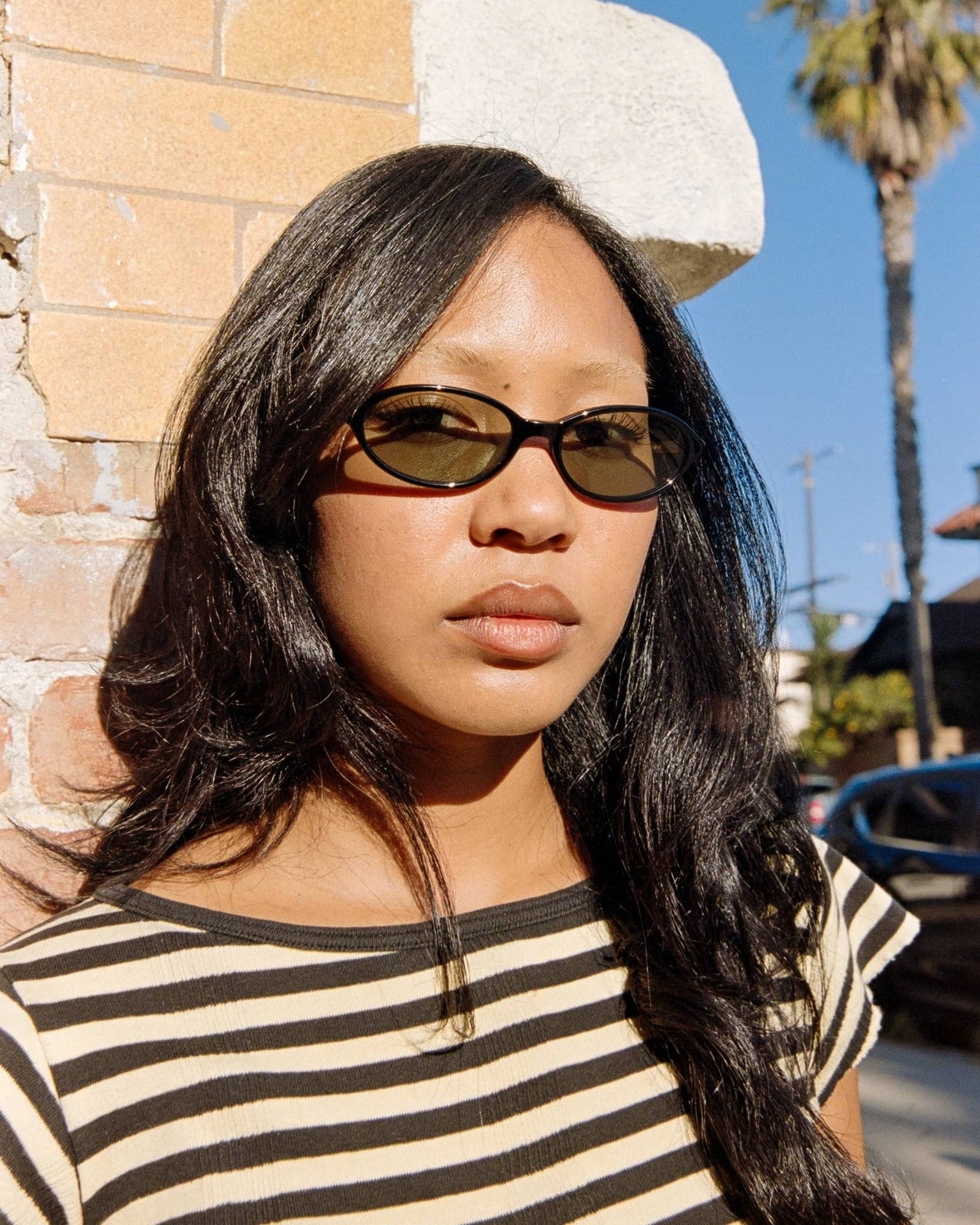 Woman wearing tortoiseshell brown oval sunglasses with tinted lenses in black and white striped shirt outdoors