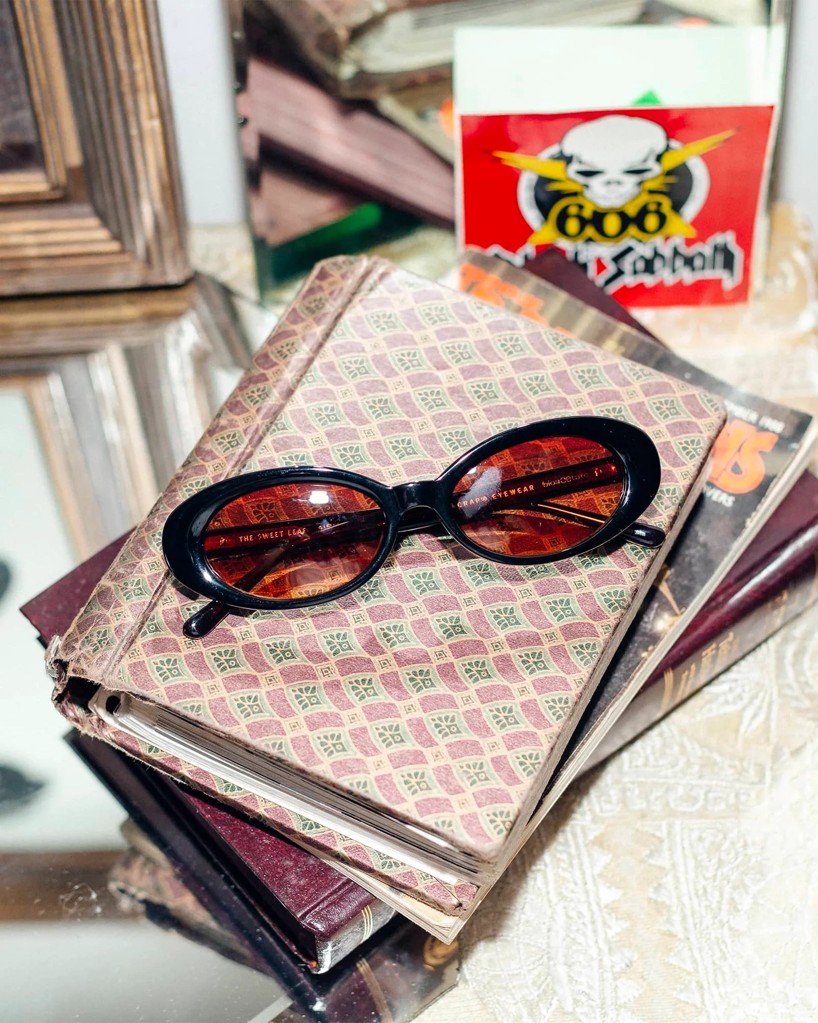 Sunglasses on top of a stack of books with a visible brand logo in the background.