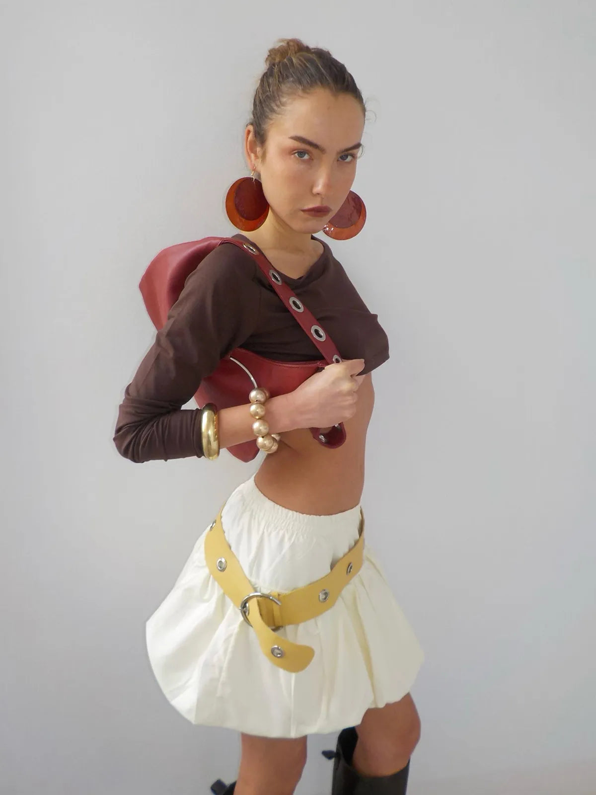 Brown cropped mesh long-sleeve top with burgundy shoulder bag, white bubble skirt, yellow utility belt, and orange hoop earrings