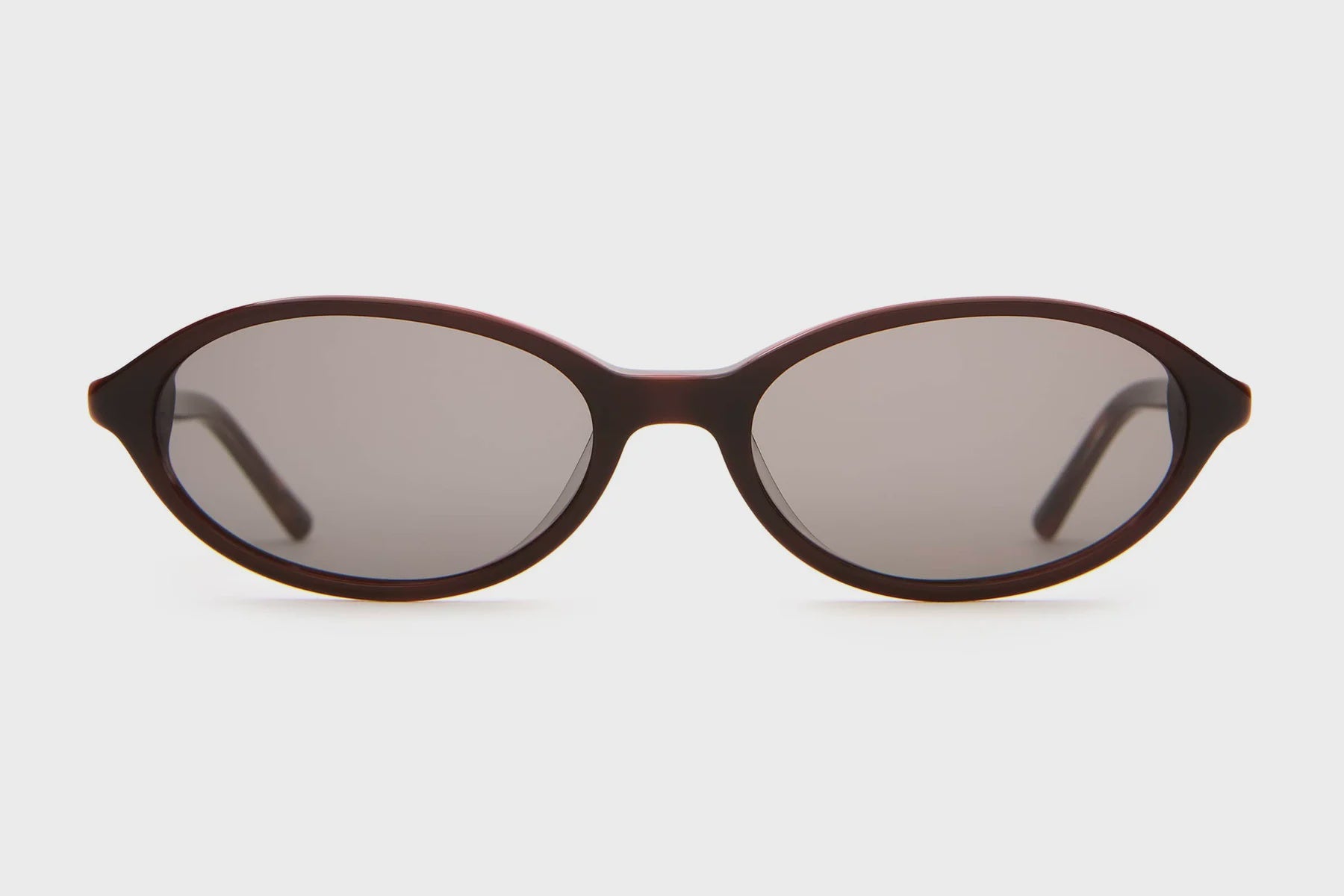 Oval brown tortoiseshell sunglasses with dark gray lenses and slim temples on white background