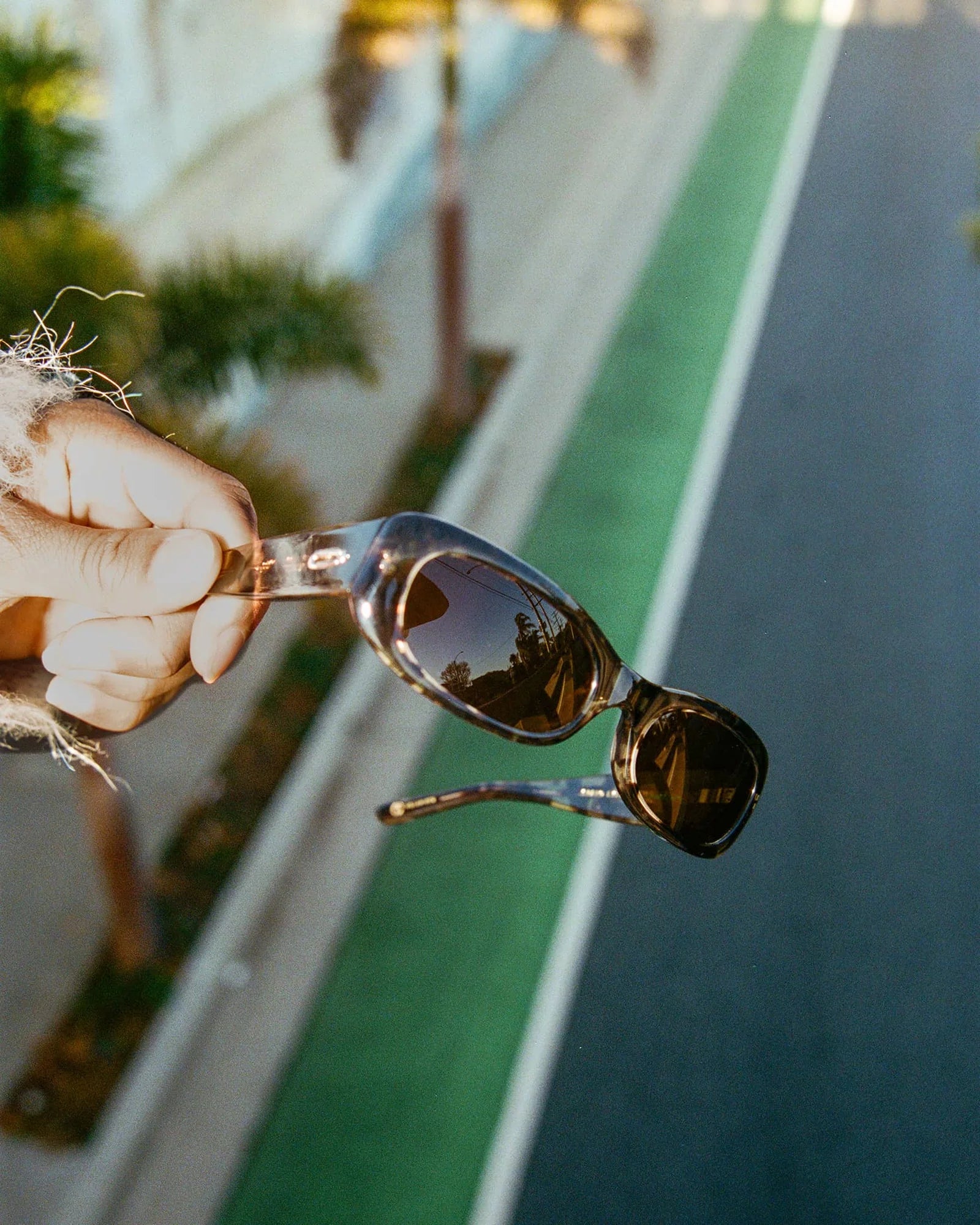 Sunglasses held by a hand with a blurred outdoor background