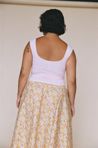 Woman wearing pink tank top and floral midi skirt, shown from behind against beige background