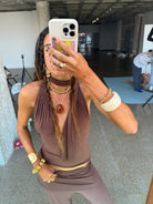 Woman taking mirror selfie wearing brown halter top and matching pants with gold jewelry and beaded phone case
