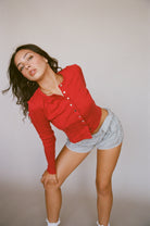 Woman wearing red button-front cardigan and blue gingham shorts in casual studio portrait pose