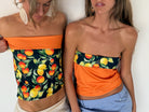 Two women wearing reversible strapless tube tops with citrus fruit print and orange color block design