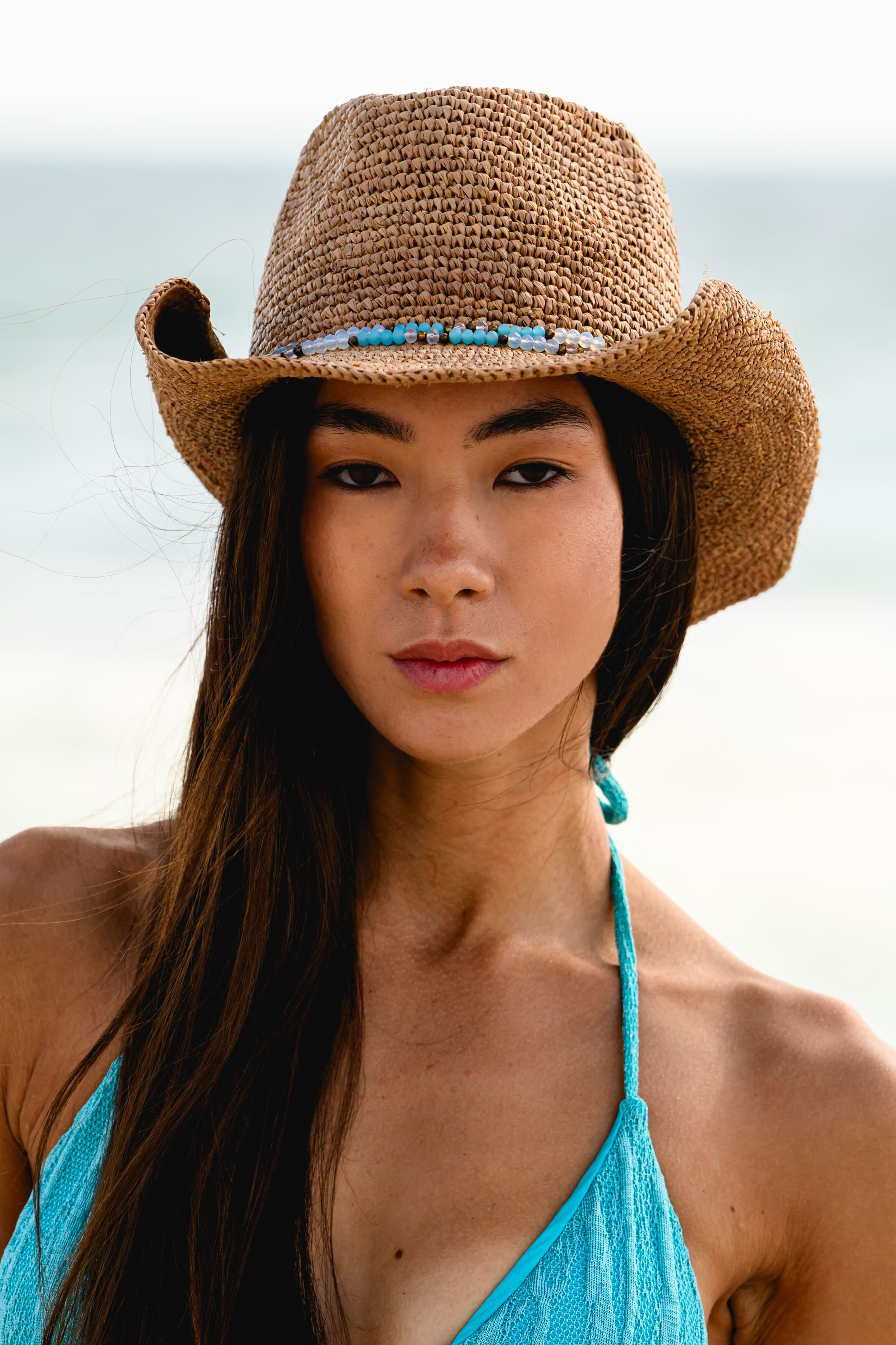 Woman wearing a straw hat and blue bikini top on a beach