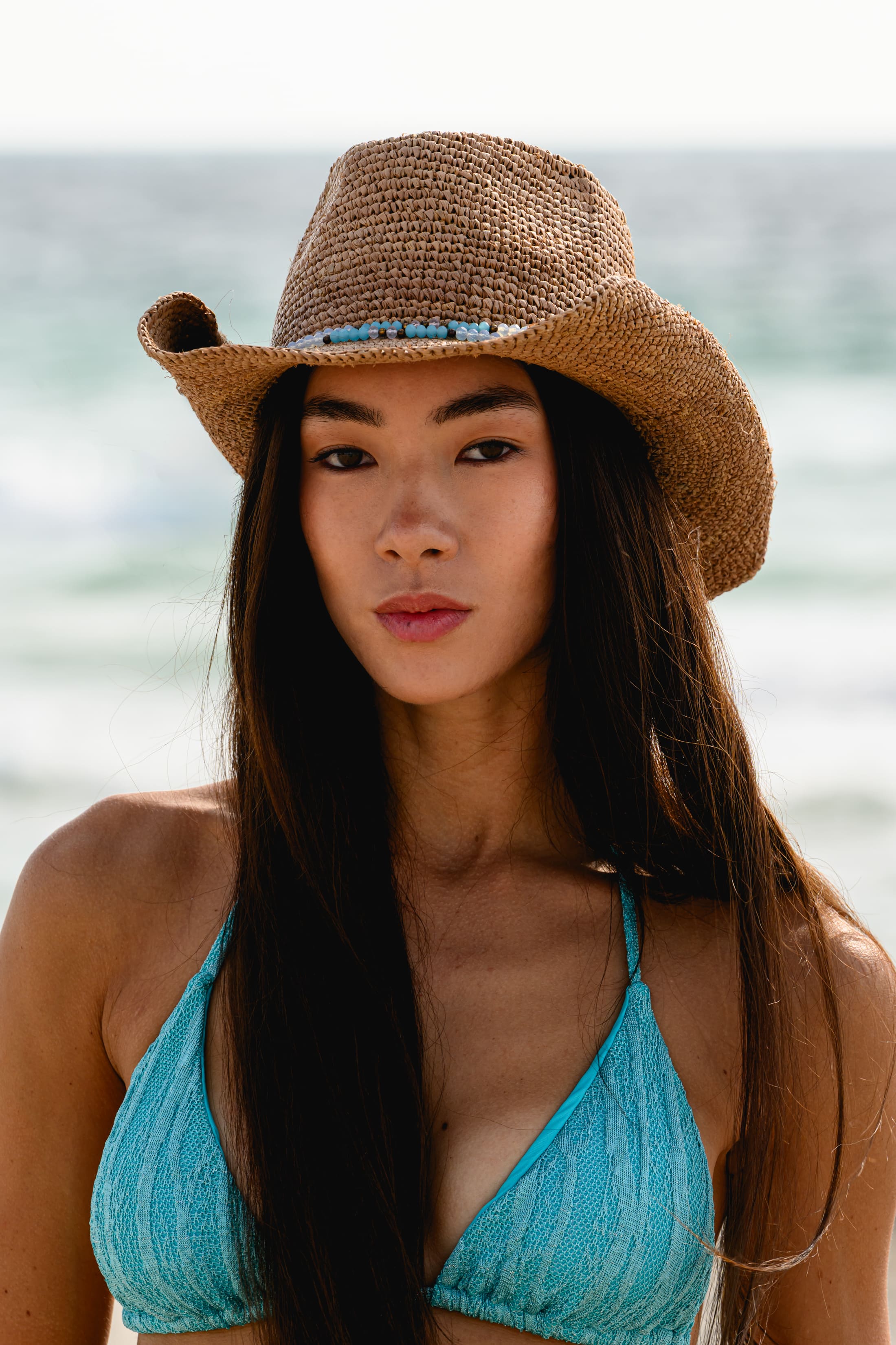 Woman wearing a straw hat and blue bikini top on a beach