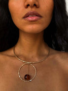 Gold circular pendant necklace with tortoiseshell bead suspended on hammered metal collar choker