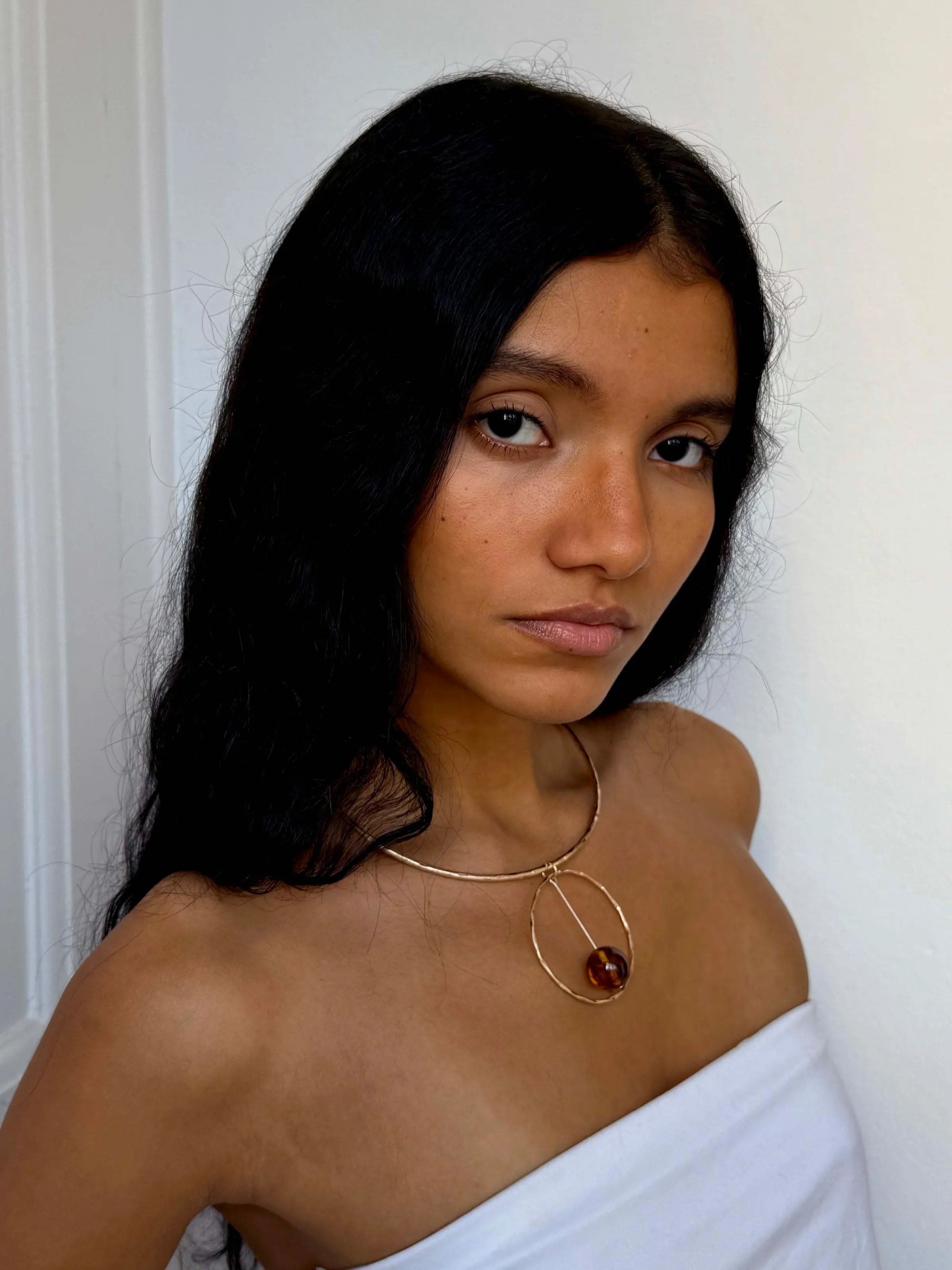 Gold geometric pendant necklace with amber stone on delicate chain, featuring circular and teardrop shapes