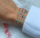Colorful beaded bracelets stack on wrist featuring turquoise, red, white and black glass seed beads on delicate cord
