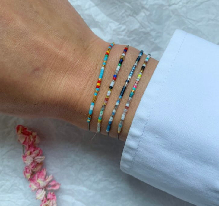 Colorful beaded bracelets stack on wrist featuring turquoise, red, white and black glass seed beads on delicate cord