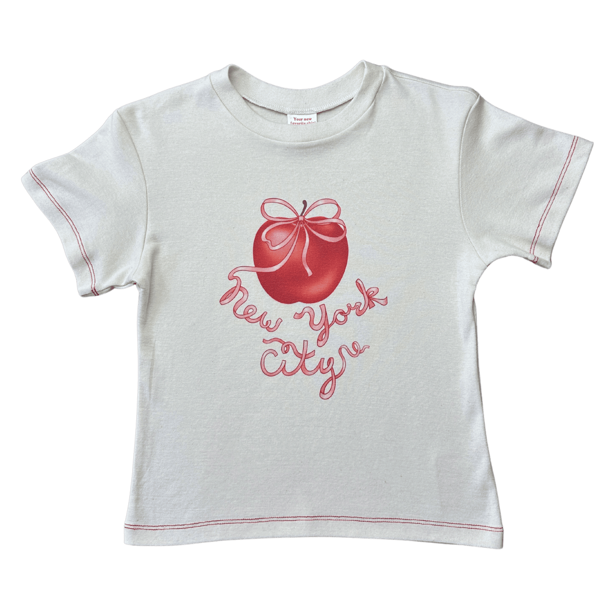 White baby tee with red contrast stitching featuring a red apple with bow and "New York City" script graphic.