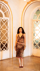 Woman in leopard print slip dress with lace trim and matching skirt, wearing gold bangles and burgundy heels in ornate room