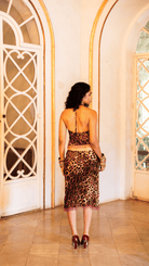 Woman in leopard print halter top and midi skirt set with fringe detail, gold bangles, and burgundy heels viewed from back
