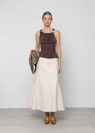 Brown cowl neck sleeveless top paired with cream midi skirt, model holding snakeskin bag wearing yellow snake-print flats