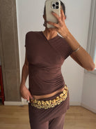 Brown ruched asymmetric top with draped detailing and short sleeves, paired with matching pants and gold coin belt