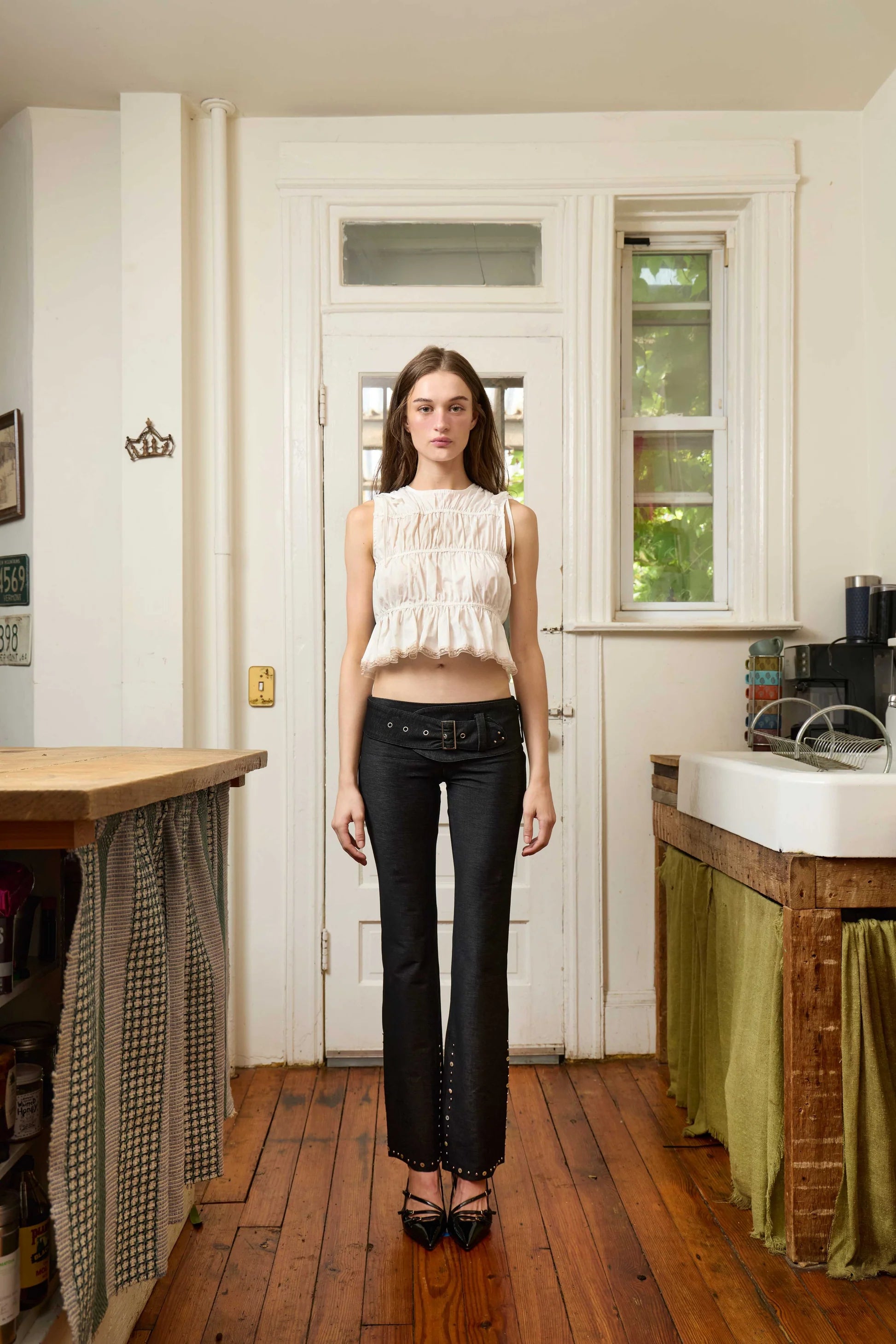 White sleeveless smocked crop top with ruffled tiers paired with black low-rise pants with studded hem detail