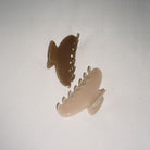 Clear acrylic or plastic hair claw clips in brown and cream colors with curved, toothed design suspended against white background