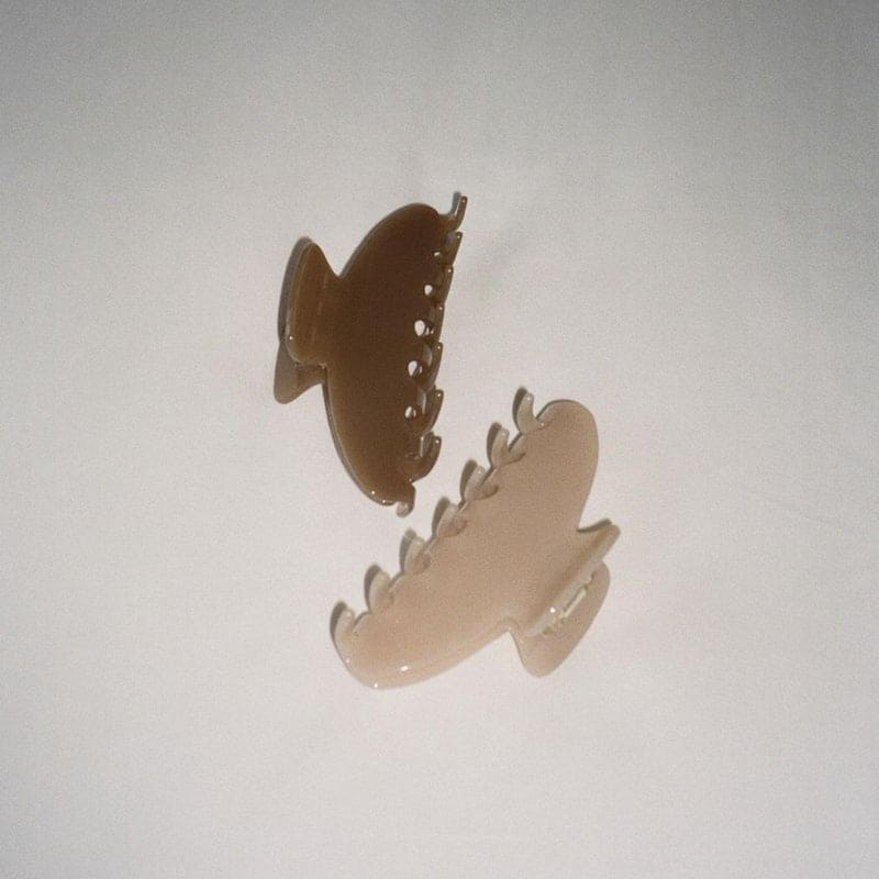 Clear acrylic or plastic hair claw clips in brown and cream colors with curved, toothed design suspended against white background