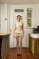 Cream sleeveless wrap top with tiered ruffle mini skirt set in soft neutral tones, featuring asymmetric draping and lace details