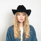 Black felt cowboy hat with wide curved brim worn by woman with blonde wavy hair in denim jacket