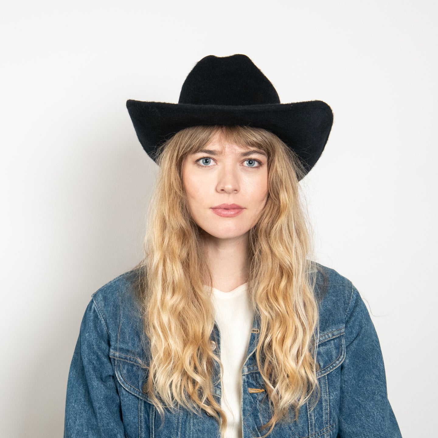 Black felt cowboy hat with wide curved brim worn by woman with blonde wavy hair in denim jacket