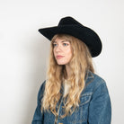 Black felt cowboy hat with wide brim worn by woman with blonde wavy hair and denim jacket