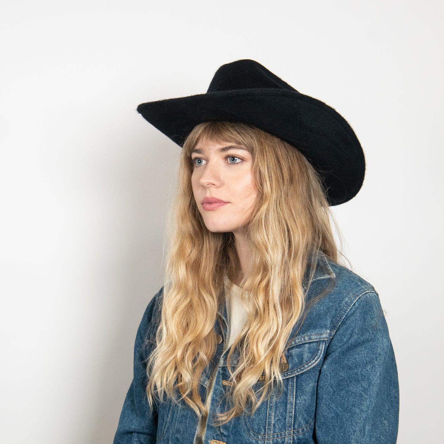 Black felt cowboy hat with wide brim worn by woman with blonde wavy hair and denim jacket