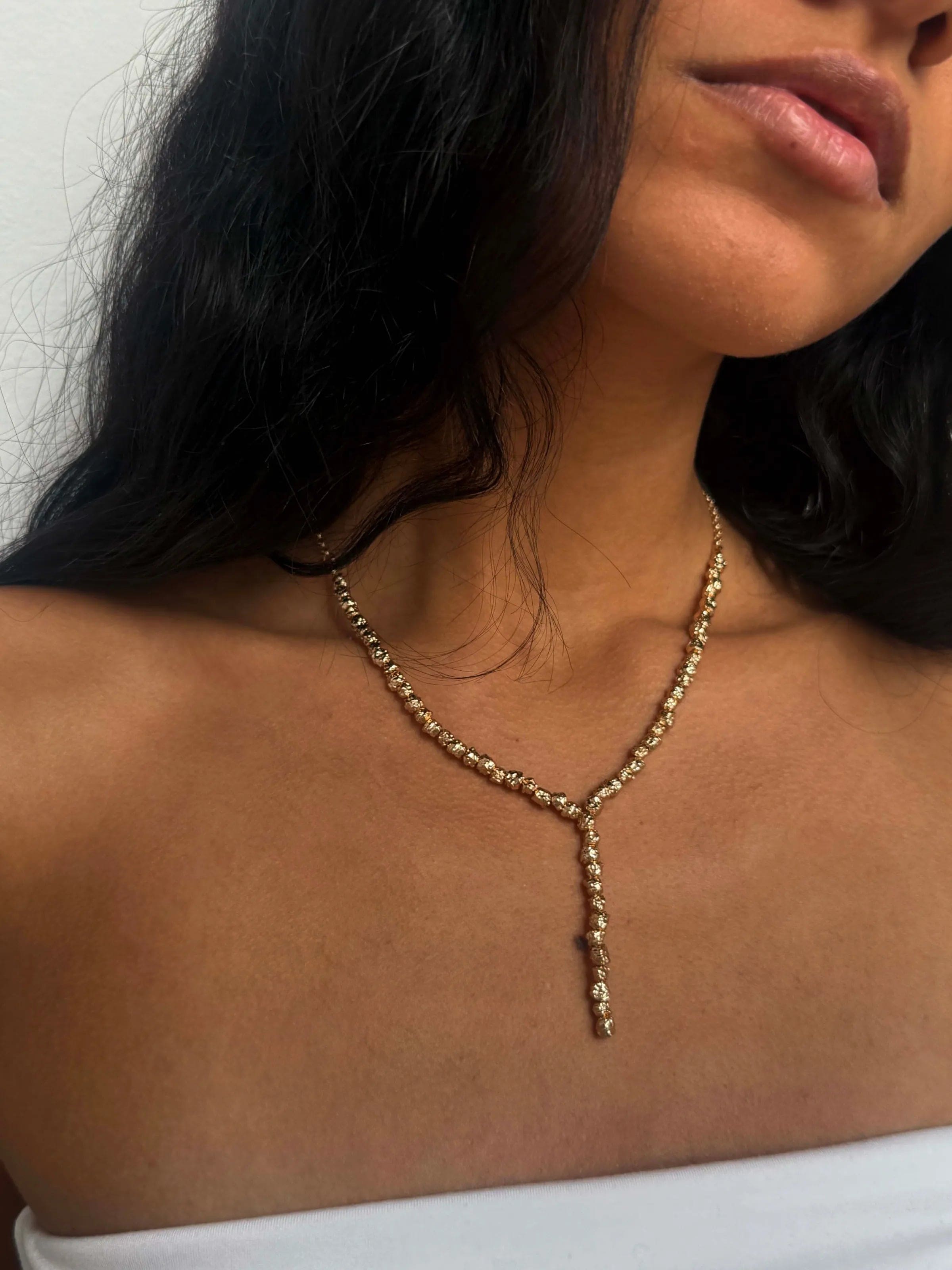 Gold Y-shaped necklace with sparkling clear crystals on delicate chain, worn on model with dark hair