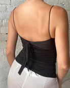 Person wearing a black tank top with thin straps against a gray brick wall.