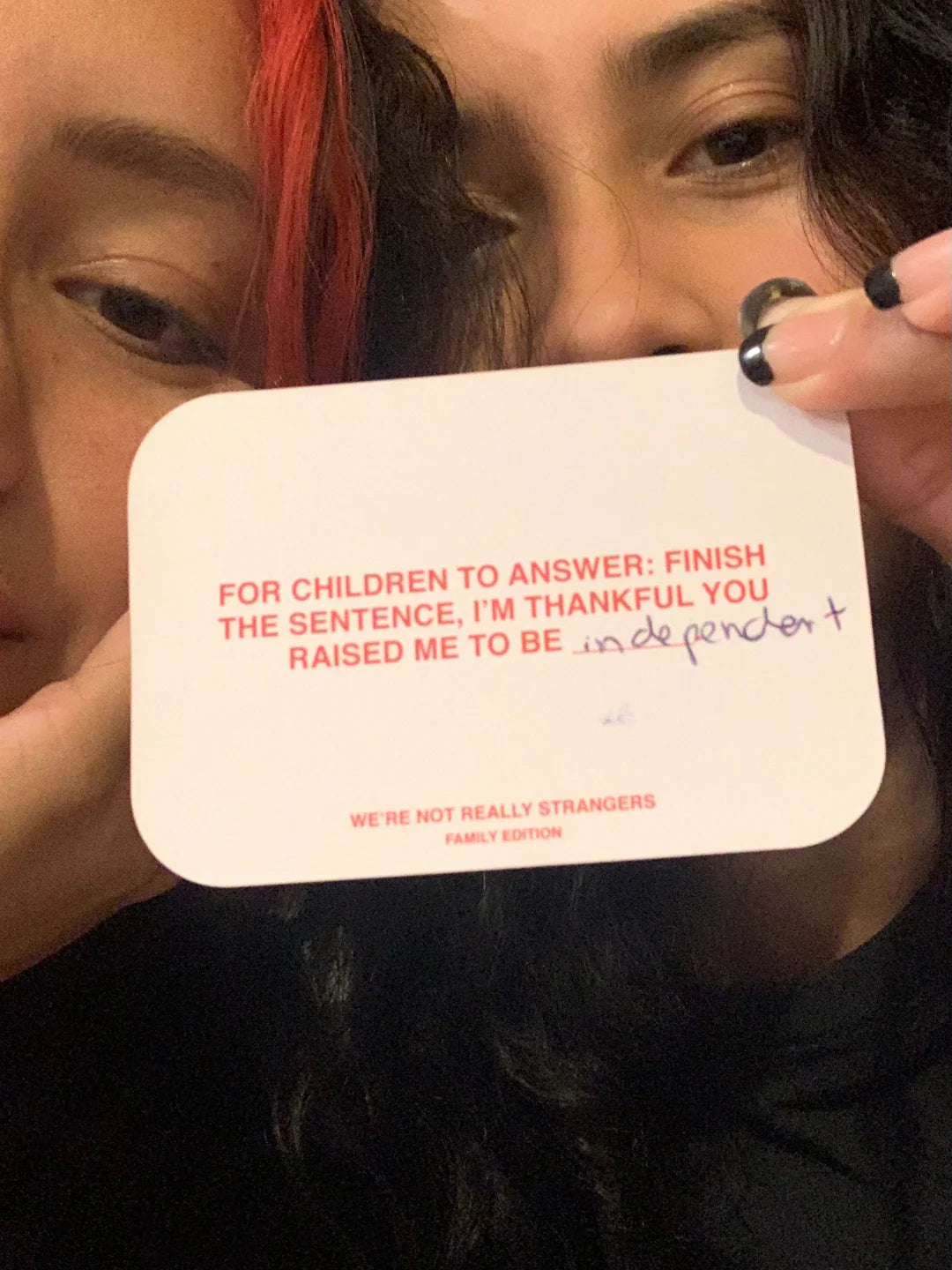 Two people holding a white game card that reads "I'm thankful you raised me to be independent" from We're Not Really Strangers Family Edition