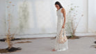 Floral printed hobo bag with fringe trim in soft beige tones, held by model in white ensemble.