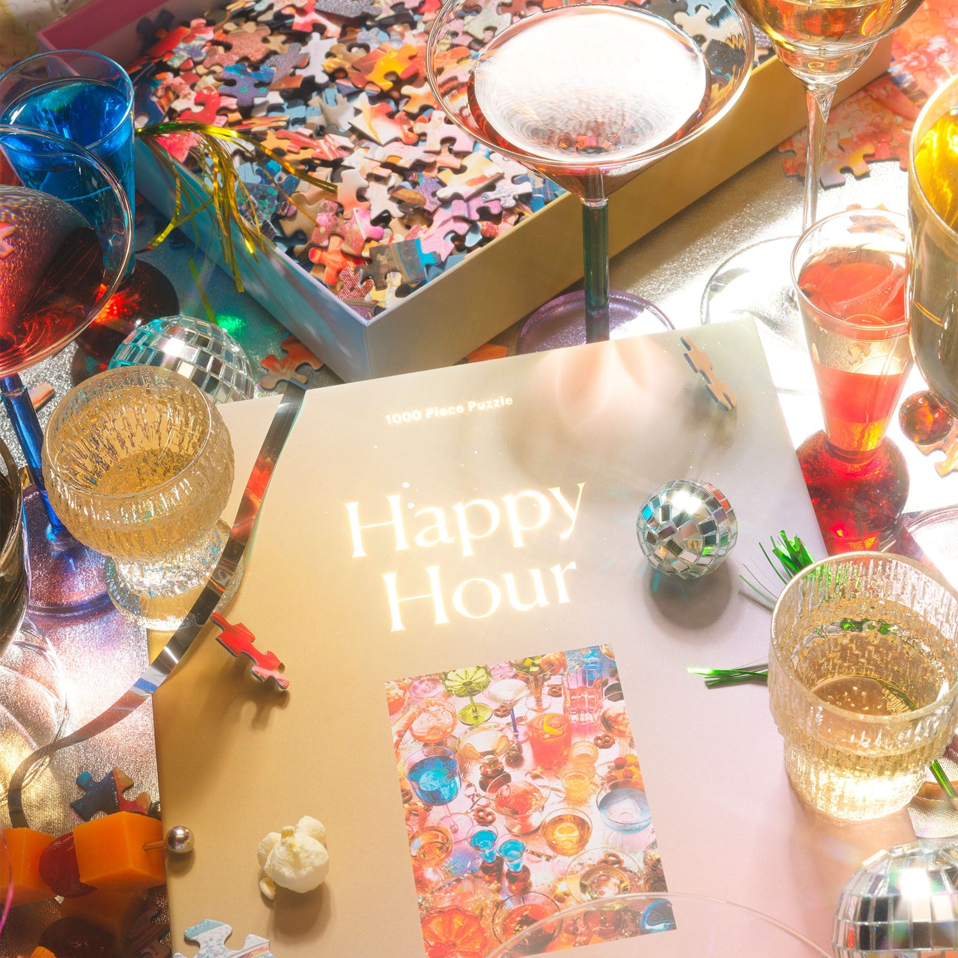 Festive happy hour table setting with colorful cocktails, disco balls, confetti puzzle pieces, and glittery decorations