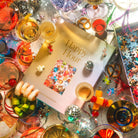 Festive Happy Hour puzzle box surrounded by colorful cocktails, disco balls, confetti, and party decorations on glittery surface